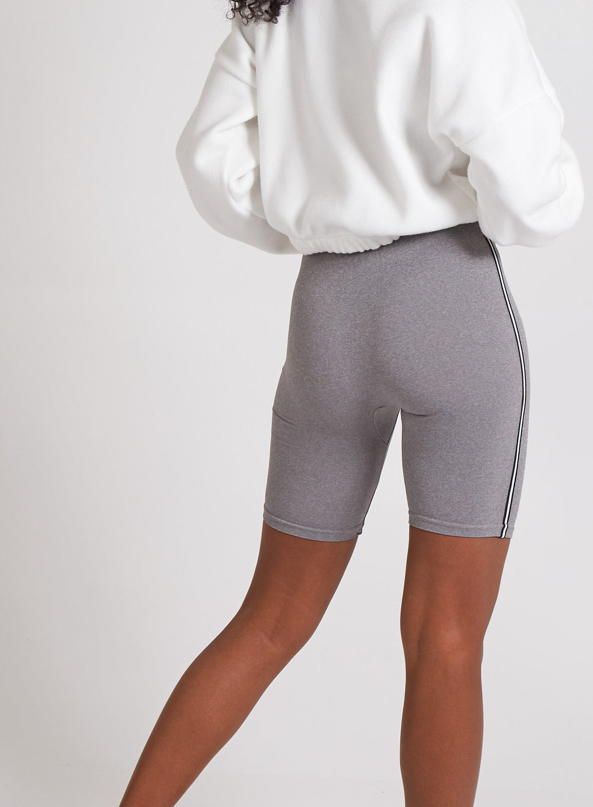 Person wearing a white sweatshirt and gray bike shorts on a plain background