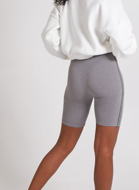 Person wearing a white sweatshirt and gray bike shorts on a plain background